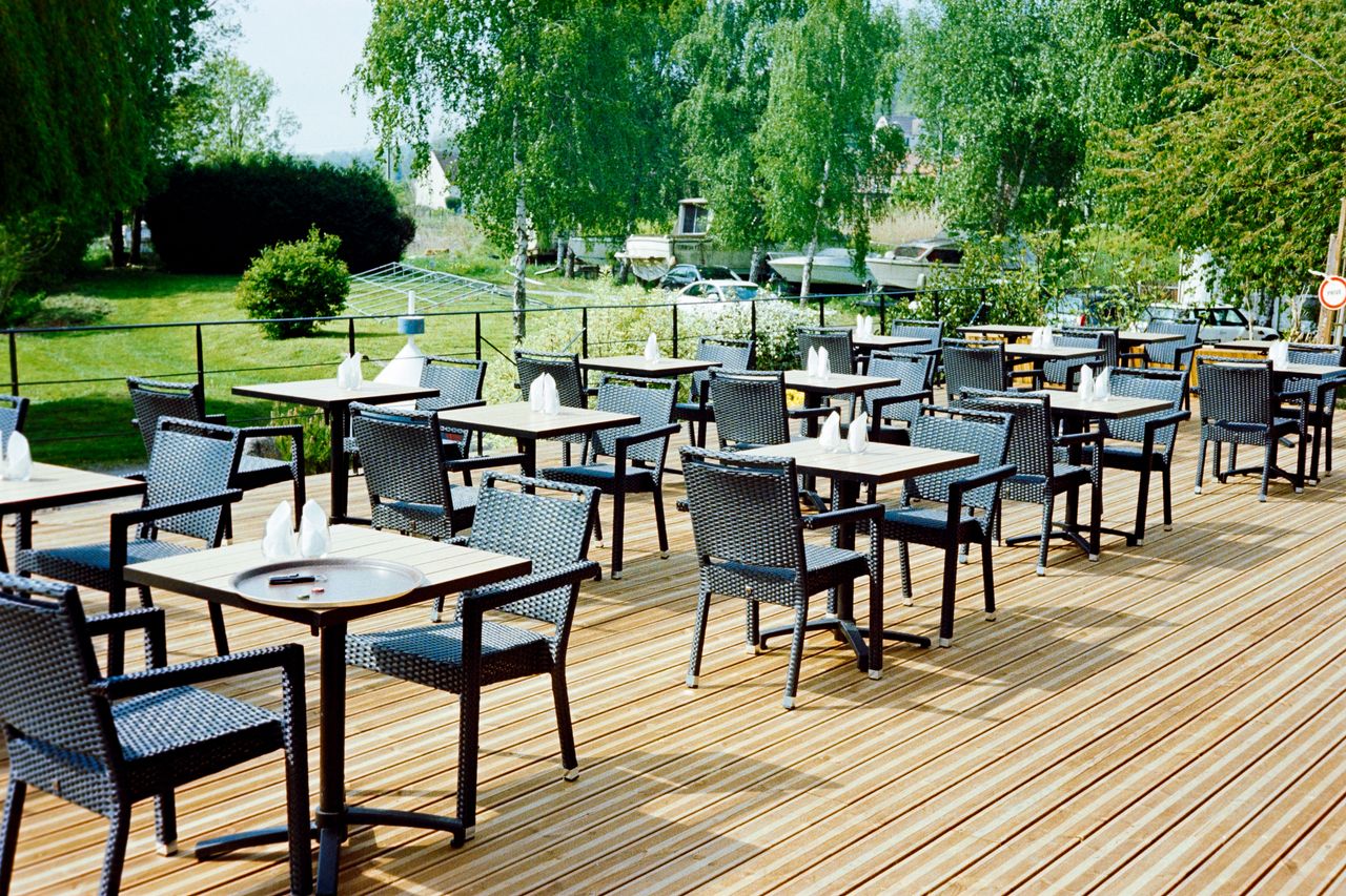 Terrasse en bois du restaurant avec tables dressées, entourée de verdure