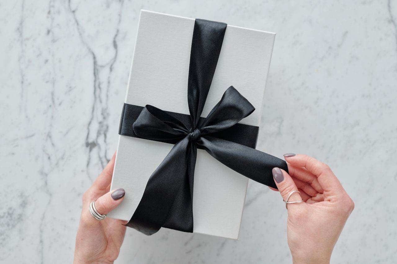 Coffret cadeau blanc noué d'un ruban noir tenu à deux mains