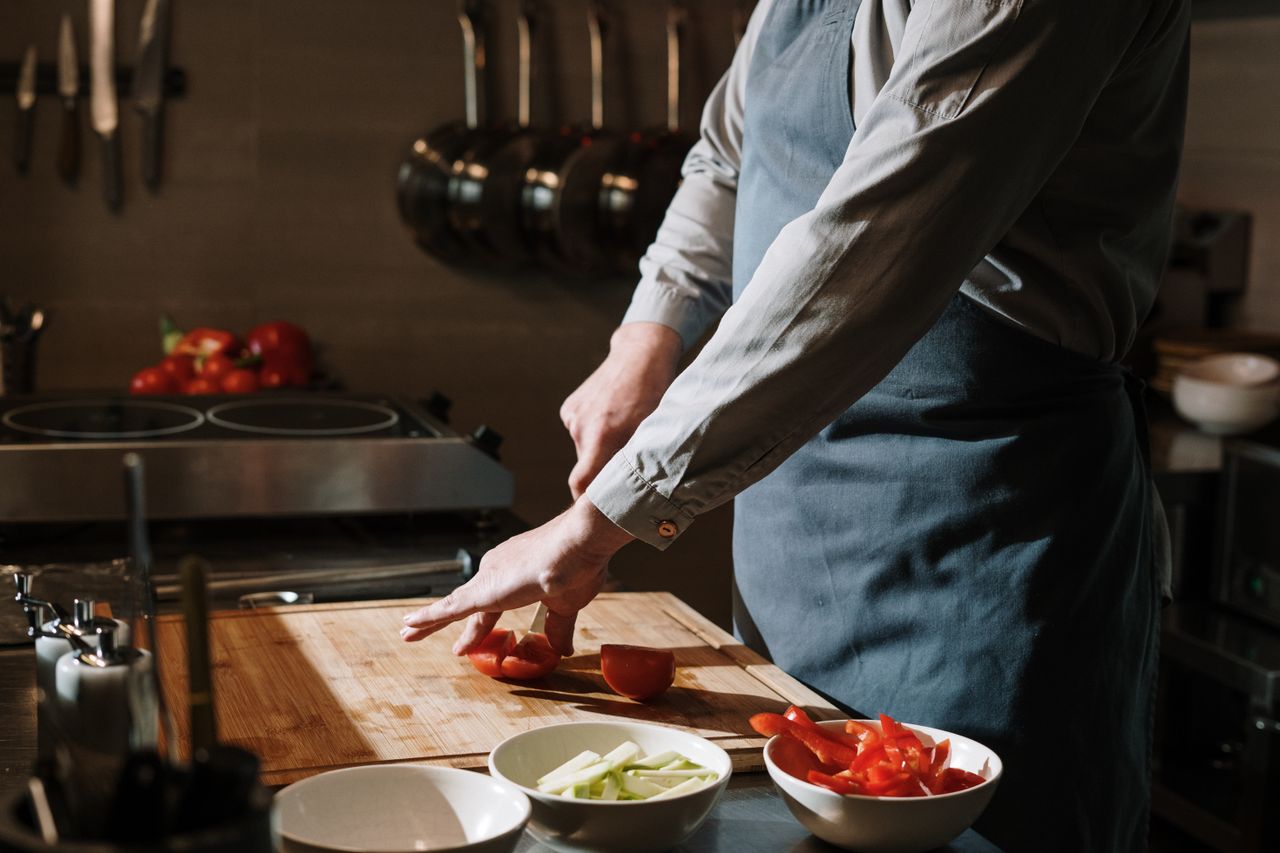 Chef en tablier découpant des légumes frais sur la planche en cuisine